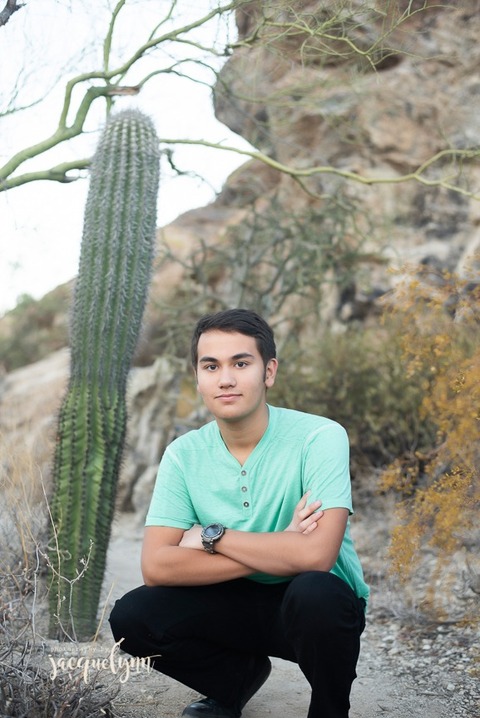 young man squatting wearing a turquoise shirt with a cactus