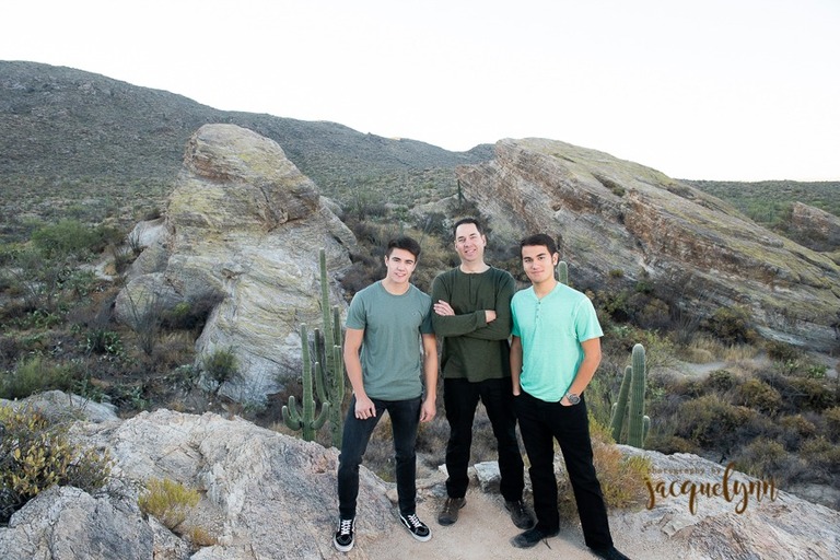 two teenage boys standing on a rock with their father