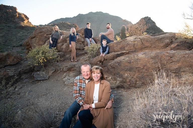 married couple sitting on ground with their children and grandchildren smaller in the background on rocks