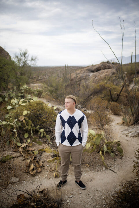 boy standing in the tucson desert for his senior pictures wearing a checkered sweater