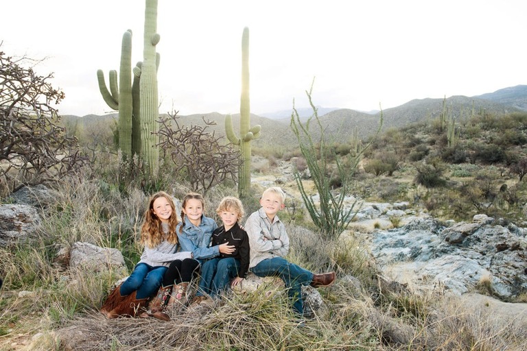 morning at tanque verde ranch tucson family photo session four siblings sitting on a rock with cactus in the background