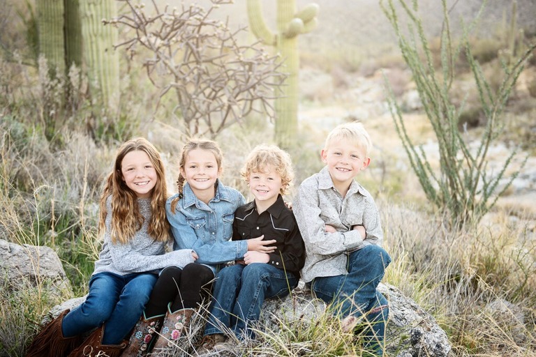 morning at tanque verde ranch tucson family photo session four siblings sitting on a rock with cactus in the background